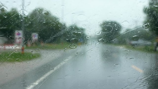 Raining, driving on the road while it rains, raindrops dripping on the glass window