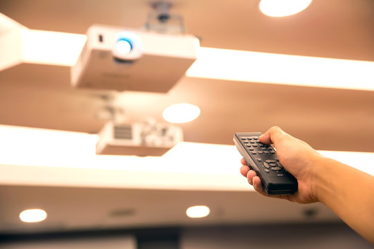 Remote turn on,Remote control in hand closeup presses button on the remote control to switch on/off the projector or blank the screen to energy saving.