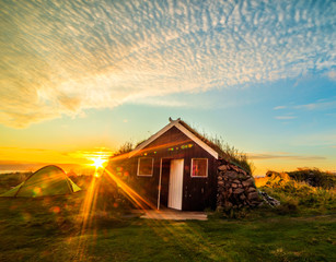 Traditional old Icelandic house with a roof with grass among the vast fields and mountains. A beautiful sky at dawn, a sunny morning. Iceland
