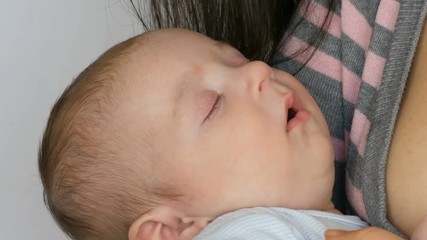 Young beautiful mother with long dark hair is holding a newborn infant baby of two months on a white background in studio