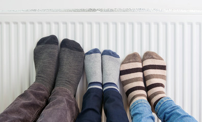 Family wears colorful pair of woolly socks warming cold feet in front of heating radiator in winter...