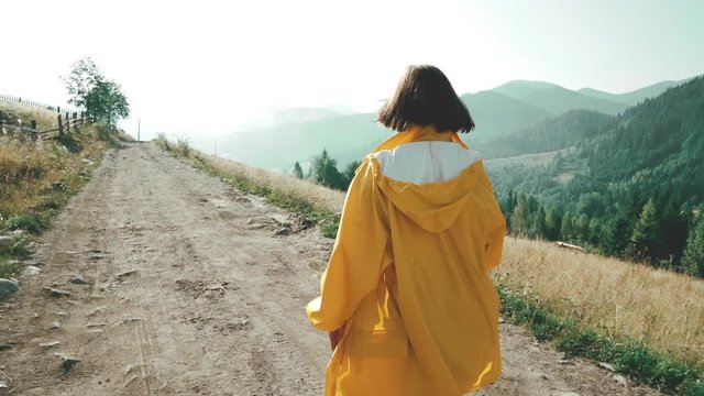 Woman in yellow raincoat walking on village off road. Early morning nature in Carpathian mountains. Travel concept