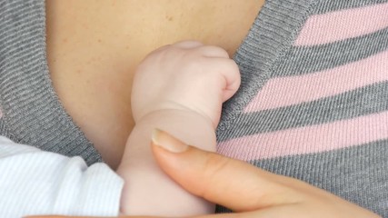 Little hand of a newborn baby of two months on the breast of the mother