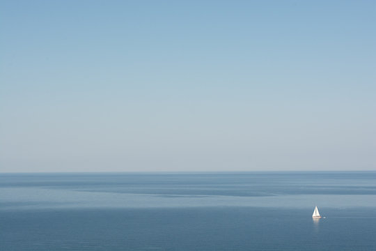 Minimalist picture of white sailboat in calm blue sea