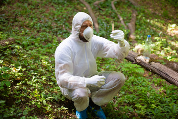 A biologist takes a sample of water from a forest stream