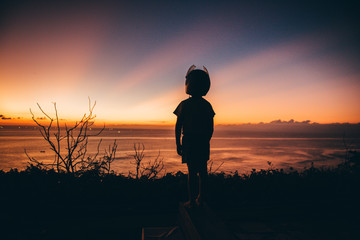 A boy in a helmet looks at the sunset at sea on the viewpoint
