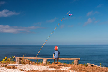 Dreaming boy sits on a bench in a helmet on the background of the sea. View point