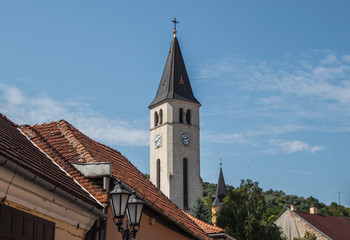 Fototapeta premium Heart of Jesus Catholic church in the old town of Tokaj wine region, Hungary, Europe. Clock tower of the 20th century neo-Romanesque Roman Catholic church and top of historical downtown buildings.