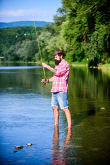 Fototapeta na wymiar Casting off. mature bearded man with fish on rod. successful fisherman in lake water. hipster fishing with spoon-bait. fly fish hobby. Summer fishery activity. big game fishing. relax on nature