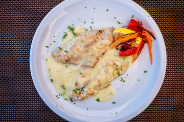 Roasted fish fillet with white cream sauce and salad garnished with parsley on the white plate, served fish dish