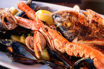 Traditional Mediterranean grilled seafood dish, plate with fish, shrimp, mussels, lemon and boiled potato, served food close up