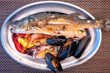 Traditional Mediterranean grilled seafood dish, plate with fish, shrimp, squid, mussels, lemon and salad, served food, top view
