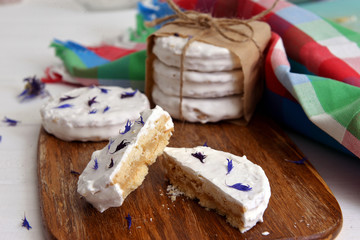 argentinean alfajores filled with dulce de leche and coated with a white meringue, decorated with dried flowers cornflower on a wooden chopping board, on white a rustic table