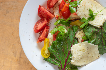 Top view on white plate full of vegetarian food - tomatoes, cheese, mangold, slices of white bread flavored with parsley, grinded  black pepper and sunflower oil