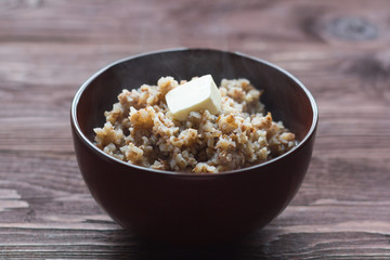 a bowl of buckwheat porridge and a piece of butter on a wooden background, tasty healthy food