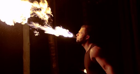 man is breathing on flaming torch for performing trick on fire show in night time