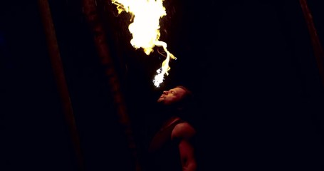 man is breathing fire in darkness, performing famous circus trick