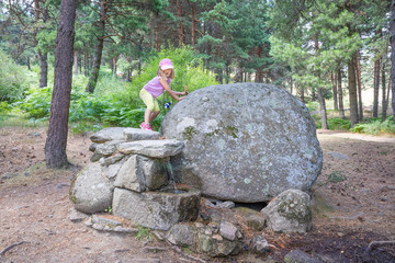 five years old blonde girl walking on rocks and above a fountain, on summer, in a forest in Guadarrama Natural Park (Madrid, Spain, Europe)