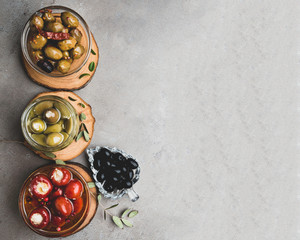 mix of olives in olive oil with herbs, red bell peppers stuffed with cheese on grey background