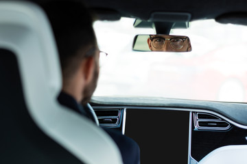 Handsome man wearing glasses looking into rear view mirror