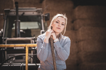 Nachdenkliche, junge Landwirtin vor einem Traktor in einer Strohlagerhalle © Countrypixel