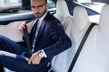 Young businessman fastening seat belt sitting on back seat