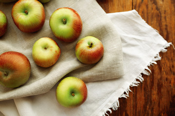 Ripe rustic apples on wooden background with beige and white linen cloth. Day.