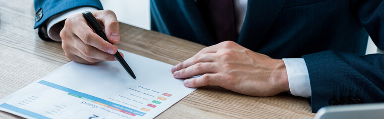 panoramic shot of man holding pen near paper with lettering on table