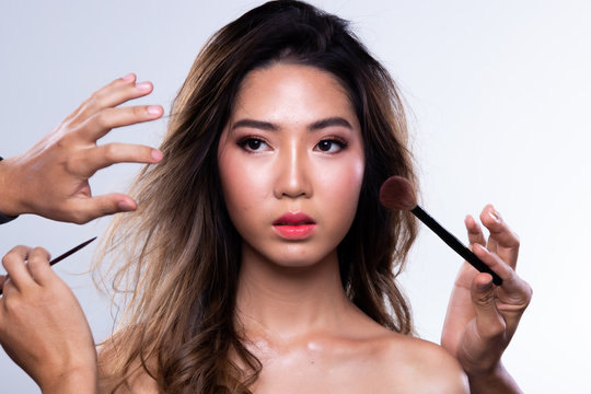 Many Hands helping Magic on Asian Woman black curl hair to be more beautiful with many people, eye shadow lipstick for many spot on big smile face,  studio lighting white background isolated