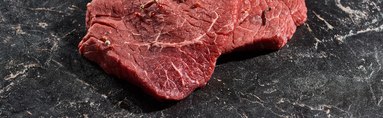 panoramic shot of fresh uncooked beef sirloin on black marble surface