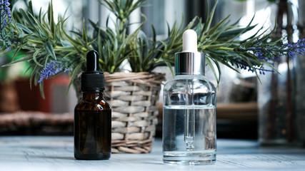 Brown, clear glasses with dropper, organic green leaves on dark background. Serum or essential oil with herbal extract