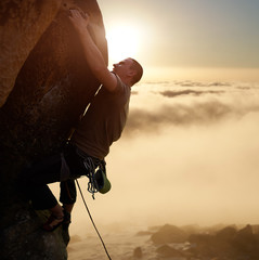 Strong brave climber blinded by sunlight on high natural rock wall. Protected climbing with rope...
