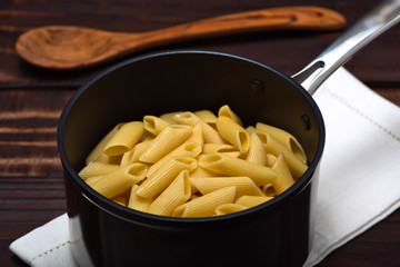 Cooked noodles (Penne Rigate) inside an professional anodized nonstick aluminum pan over a napkin on a vintage wooden surface.