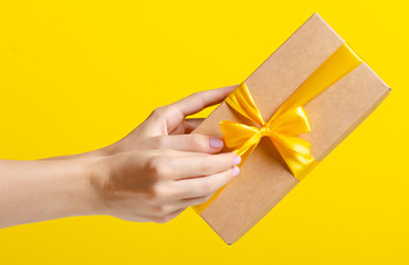 Gift box with yellow ribbon in hand on yellow background
