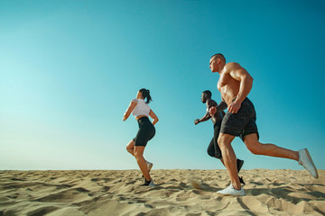 Group of young sportsmens women and men, fit athletes runners running on the sky background....