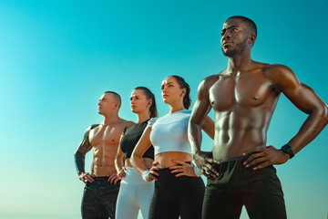 Group of four young sportsmens women and men, fit athletes are standing on the sky background before run. Healthy lifestyle and sport. Friends in black and white sportswear. Fitness concept.