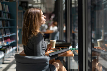 Caucasian girl student reads book in institute library and drinks coffee