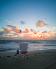 people sit on lifeguard stand with people playing surfboard in background with sunset in scarborough beach western australia