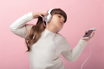 girl listening to music in headphones. student in white sweater and ponytails on pink background