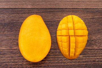 Fresh mango, beautiful chopped fruit with green leaves on dark wooden table background. Tropical fruit design concept. Flat lay. Top view. Copy space