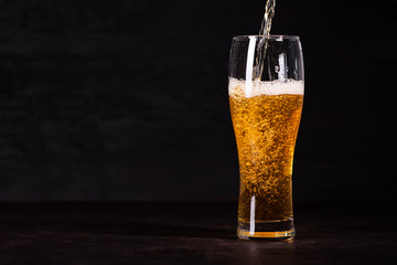 Pour beer in beer glass on dark wooden background. October fest background
