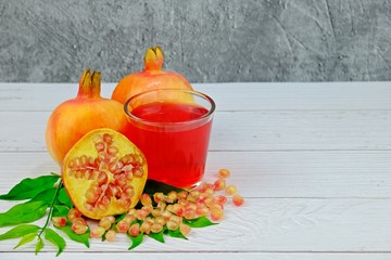 Pomegranates fruit and juice with leaves on white wooden table having concrete as background.