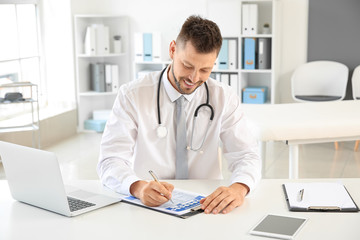 Fototapeta premium Male doctor working at table in clinic