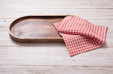 Black plate or tray, or pizza board, with tablecloth on wooden table. Top view mockup