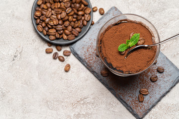 Portion of Classic tiramisu dessert in a glass cup on stone serving board on concrete background