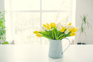 A bouquet of tulips in a pot in the form of a teapot on a white table. Taken in warm daylight.