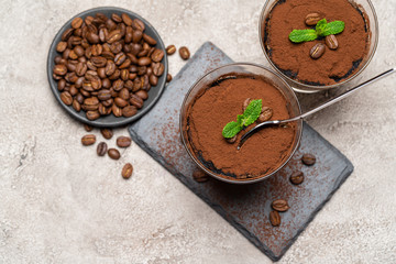 Portion of Classic tiramisu dessert in a glass cup on stone serving board on concrete background
