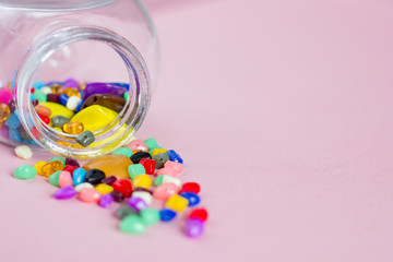 Multi-colored beads in a glass jar for needlework on a pink background