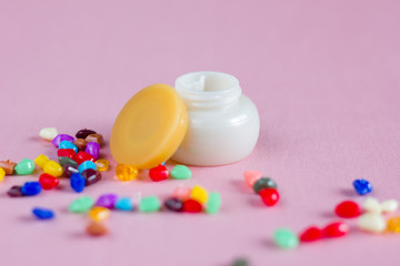 Jars with face cream on a pink background and multi-colored pebbles