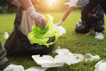 two people keeping garbage plastic bottle into black bag at park in morning light